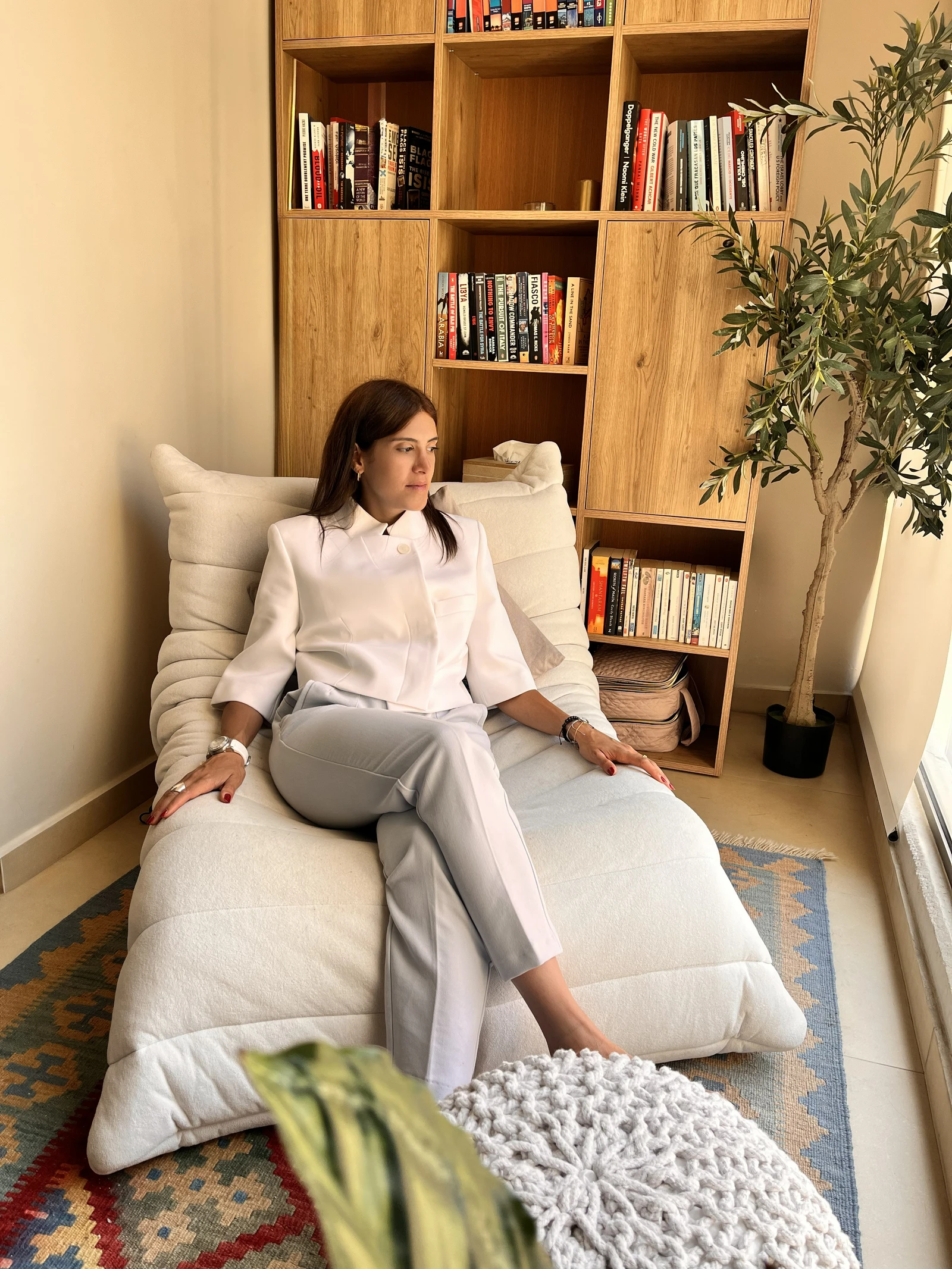 Amanda Kobersy seated in a warm interior with oak shelving and an olive tree